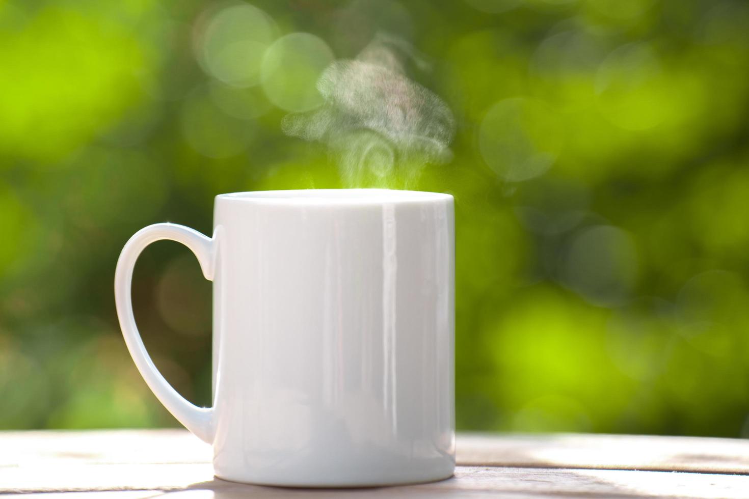 vit keramisk kaffemugg på trägolvet, grönt träd bokeh bakgrund. mjukt fokus.effekt för grunt fokus. foto