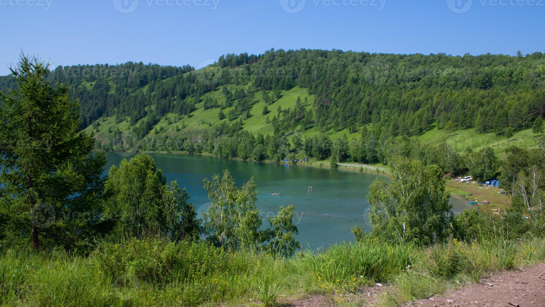 pittoresk sjö omgiven av berg med grönt gräs och träd. foto