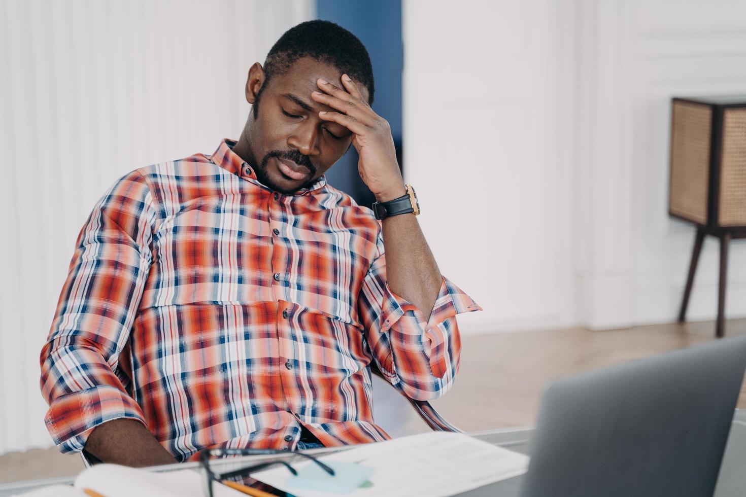 trött afrikansk amerikansk man lider av huvudvärk på laptop tänker på affärsproblem. stress på jobbet foto
