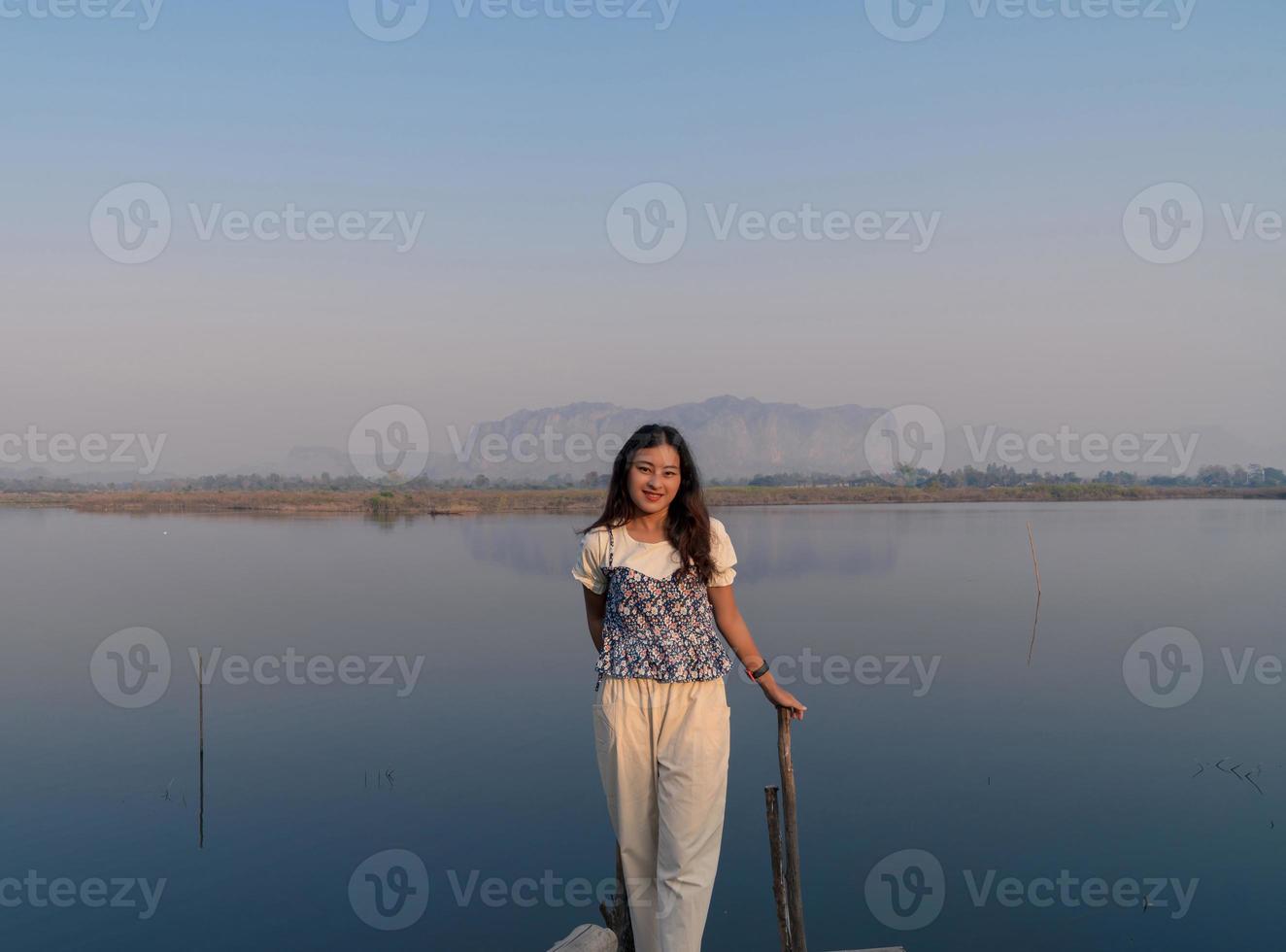 le glad asiatisk kvinna turist koppla av med vackert lugnt bergslandskap med främre sjöreflektion på morgonen med dimmig luft foto