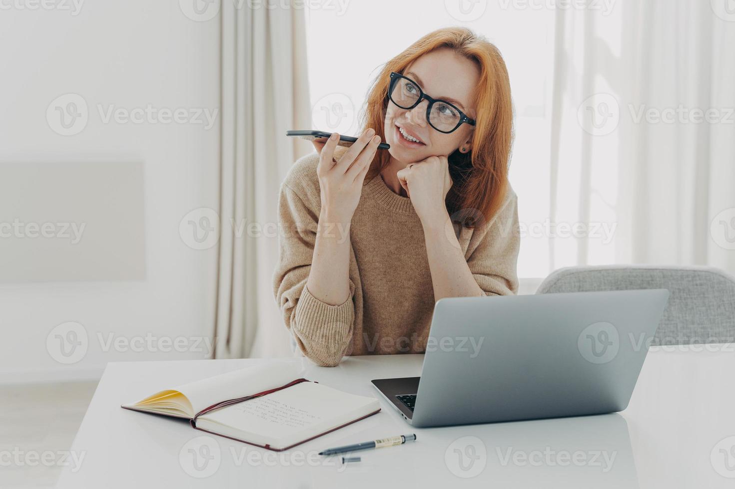 kvinnlig frilansare spelar in röstmeddelande sitter vid skrivbordet gör anteckningar i anteckningsblock foto