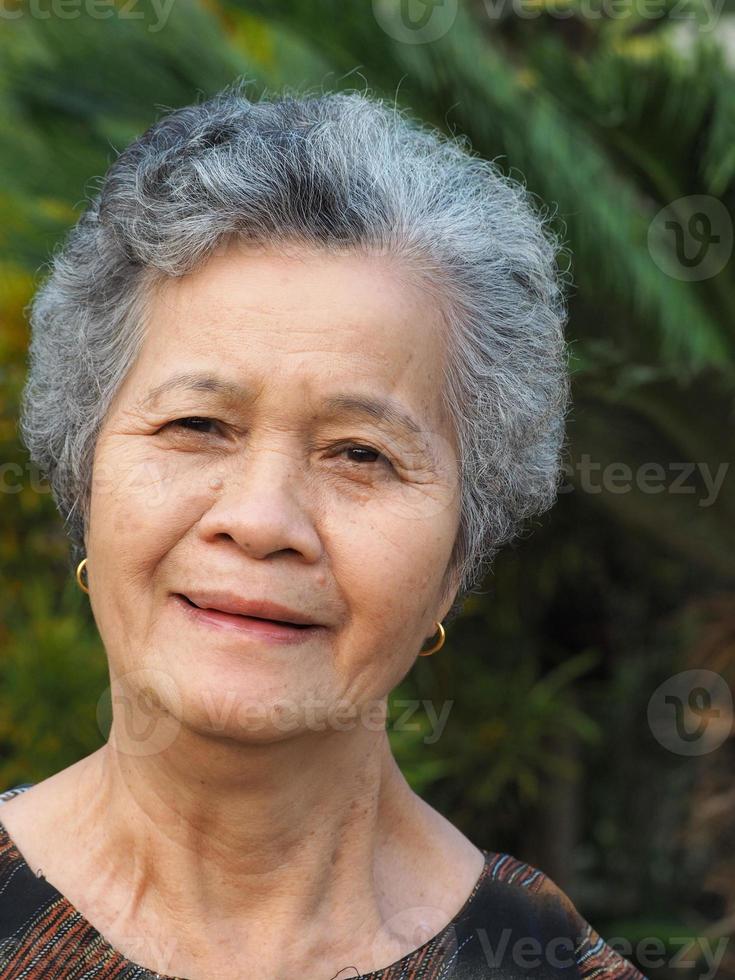 porträtt av en äldre kvinna som ler och tittar på kameran när hon står i en trädgård foto