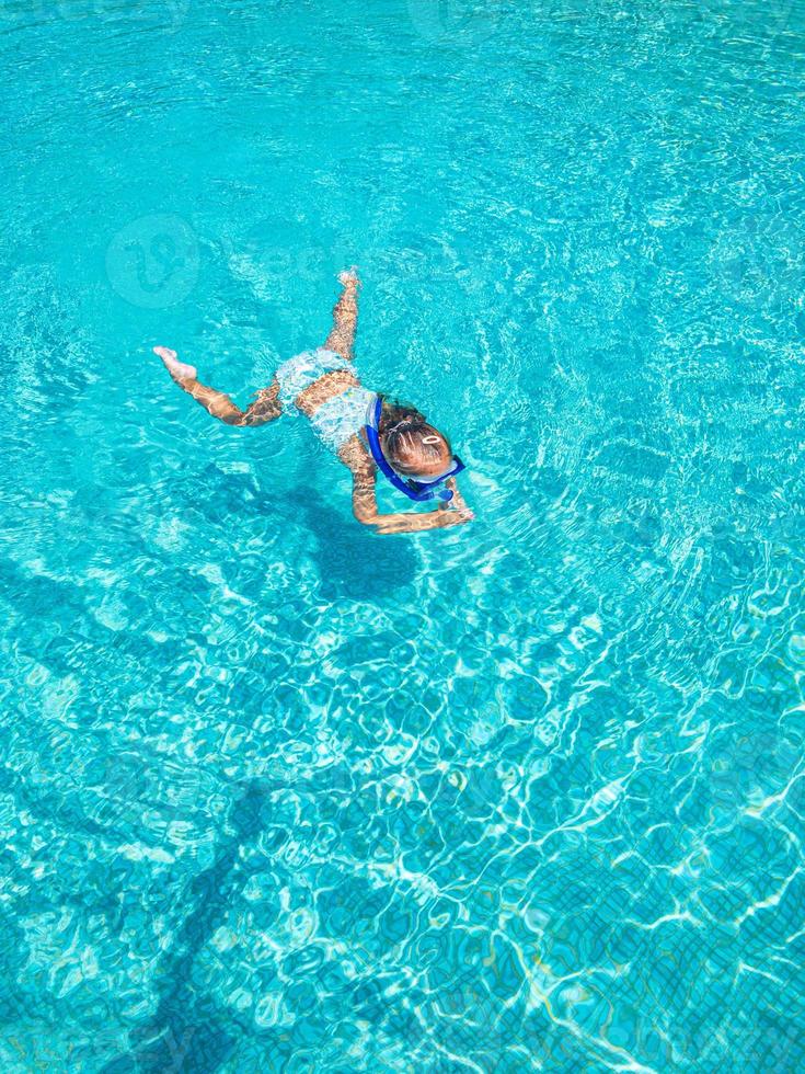 söt liten flicka i klar pool simmar under vattnet med snorkelutrustning. sommarlov, familjeresor foto