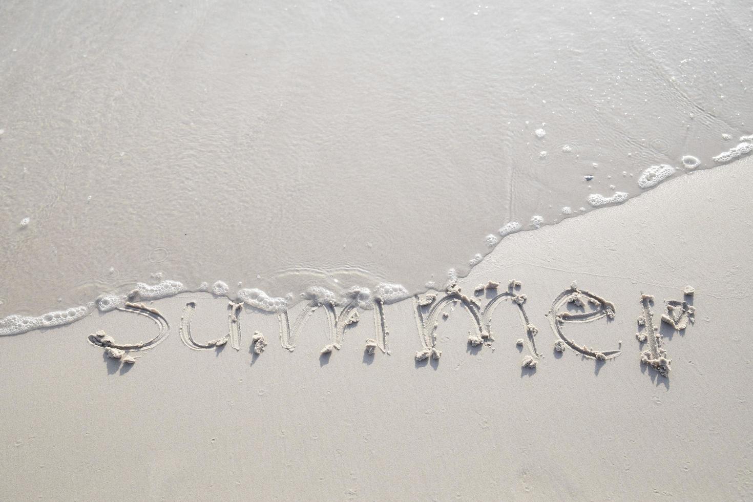ordet sommar hand skriven i sanden. närbild sand textur på stranden på sommaren. semester, semester koncept, foto