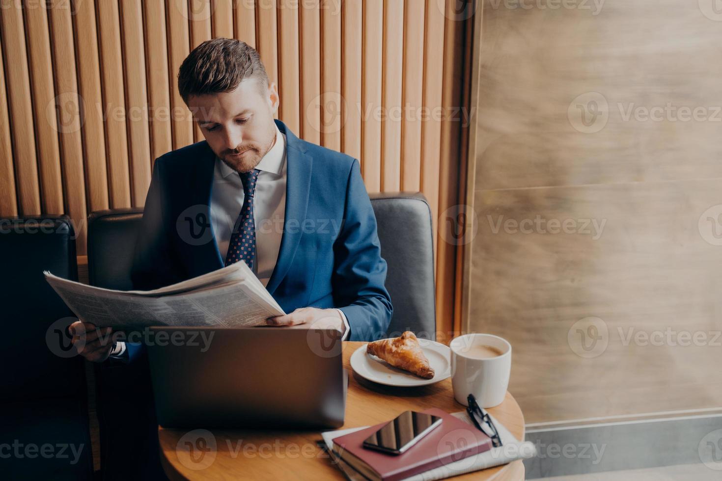 ung man entreprenör i formell smoking läser tidningen i café foto