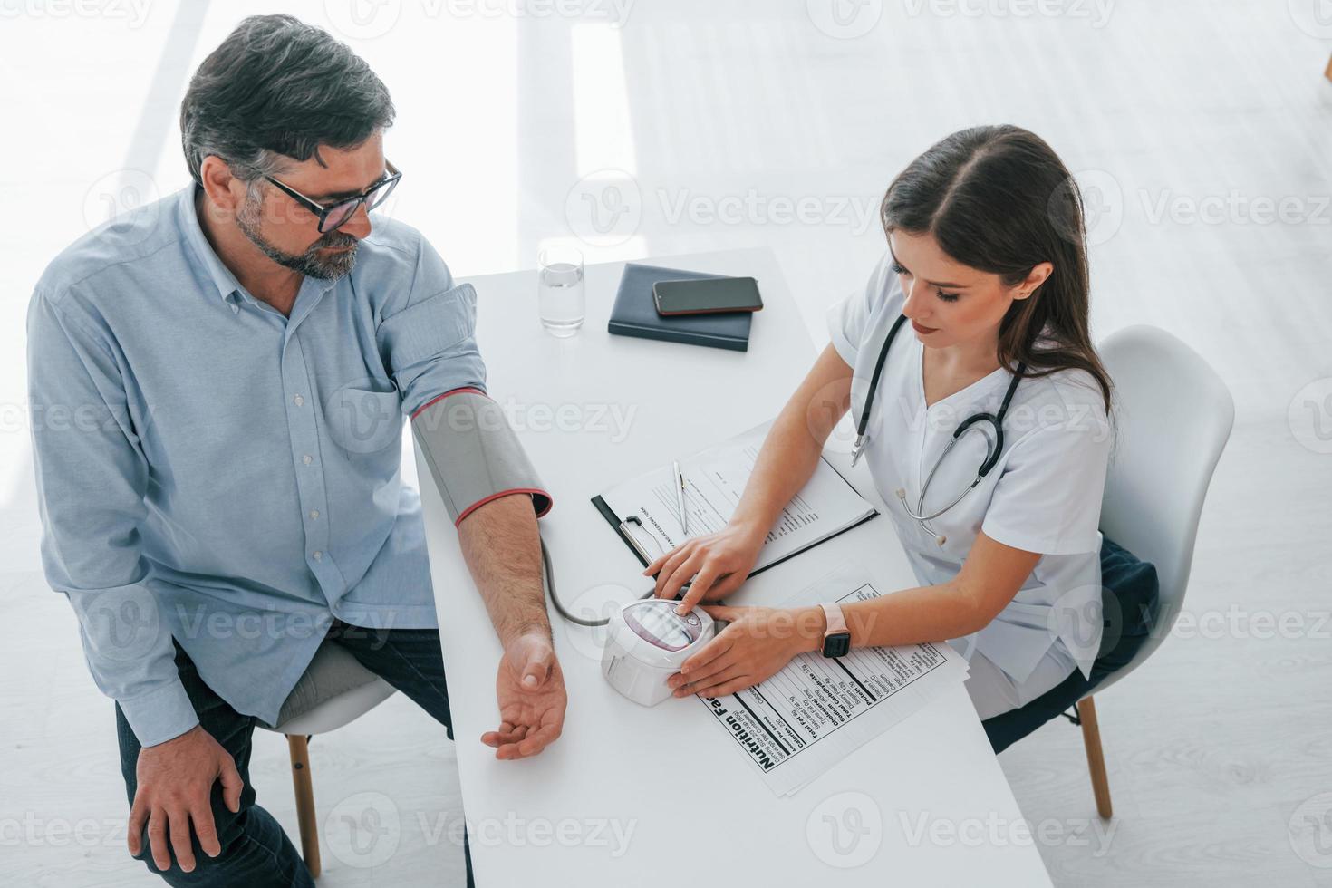 kvinnlig läkare mäter mannens blodtryck. professionell medicinsk arbetare i vit rock är på kontoret foto