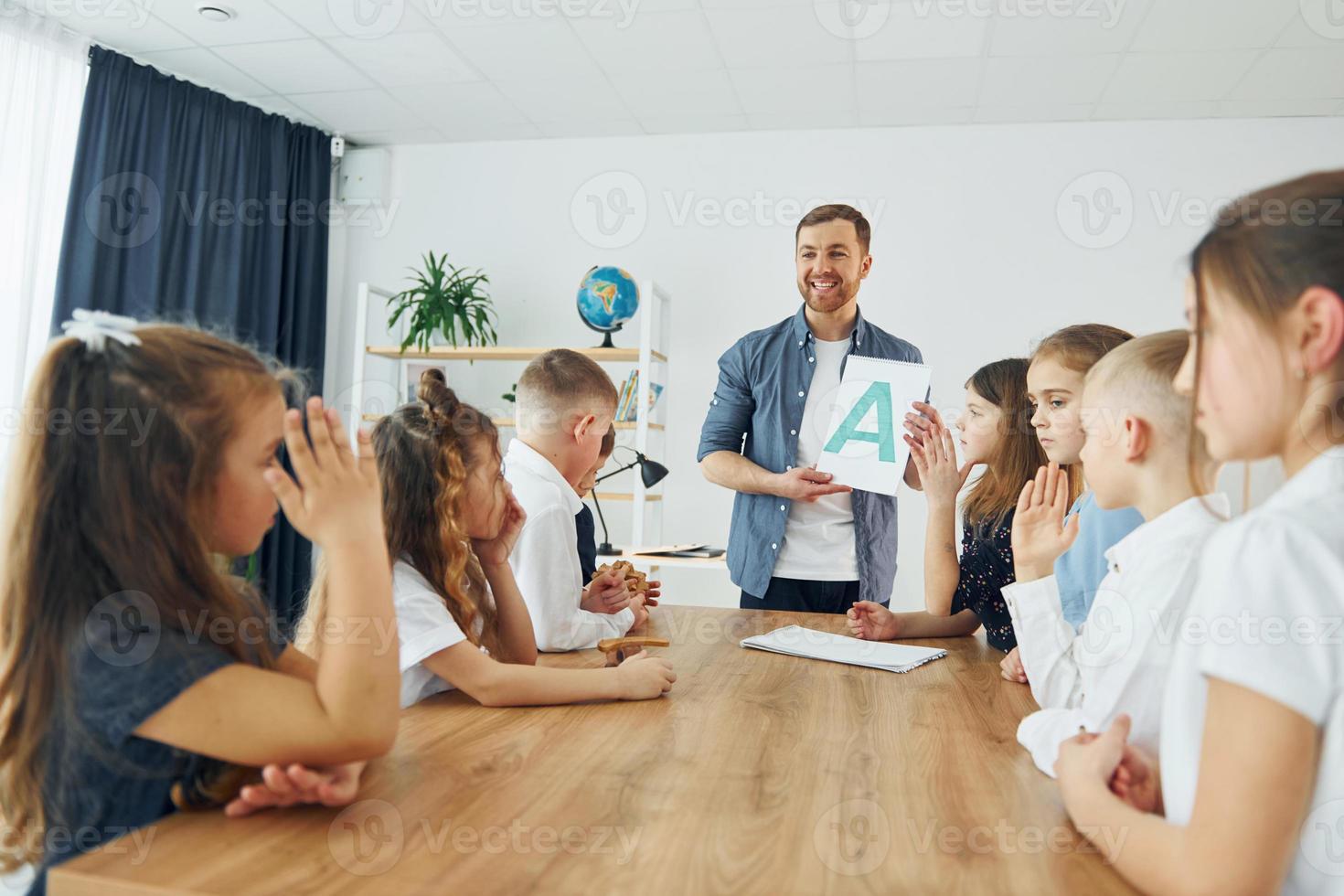 lära sig en ny bokstav. grupp barn elever i klassen i skolan med lärare foto