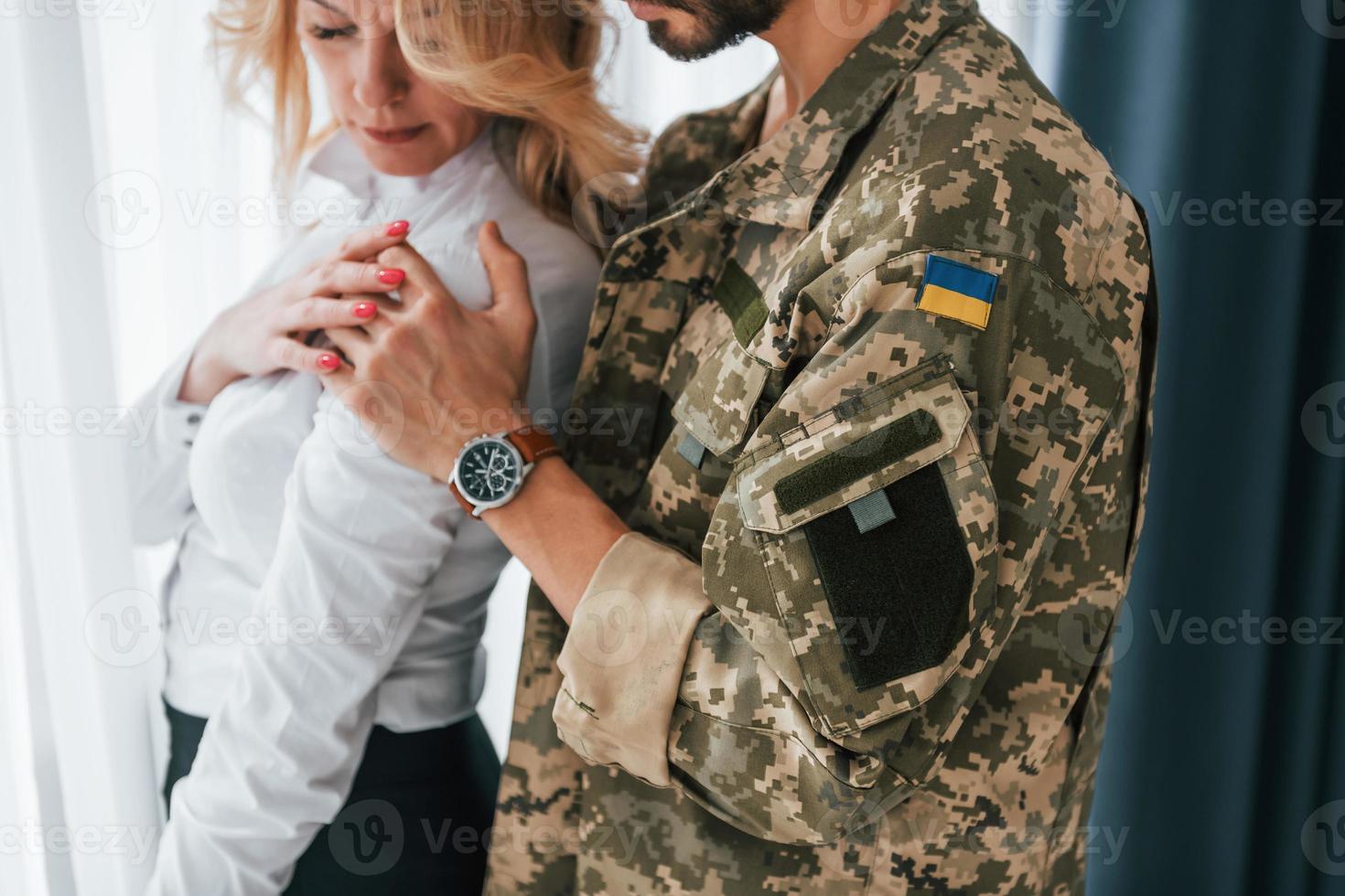 Ukrainas flagga. soldat med sin fru som står inomhus och omfamnar foto