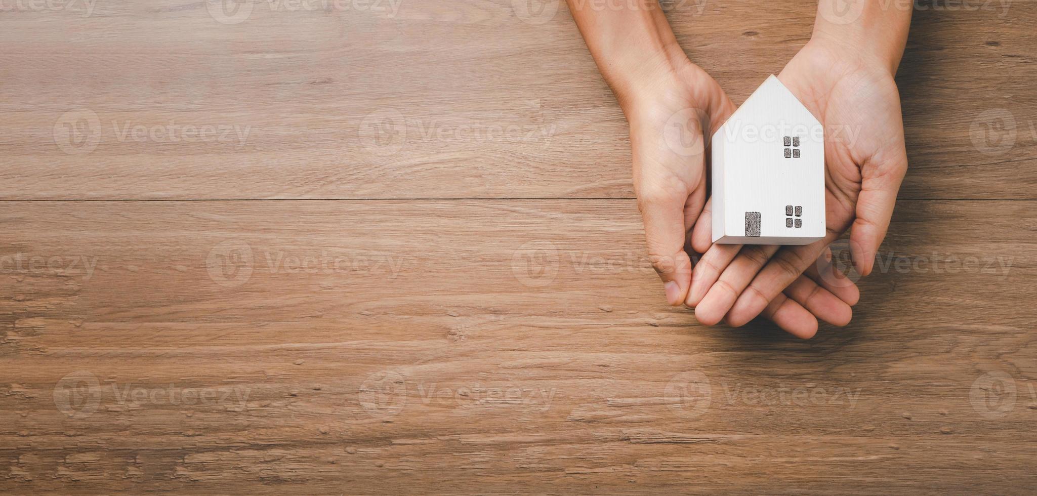 kvinna hand som håller trähus på gul bakgrund, hemlösa bostäder och hemskydd försäkring koncept, internationella dagen för familjer, hemundervisning, ovanifrån. foto