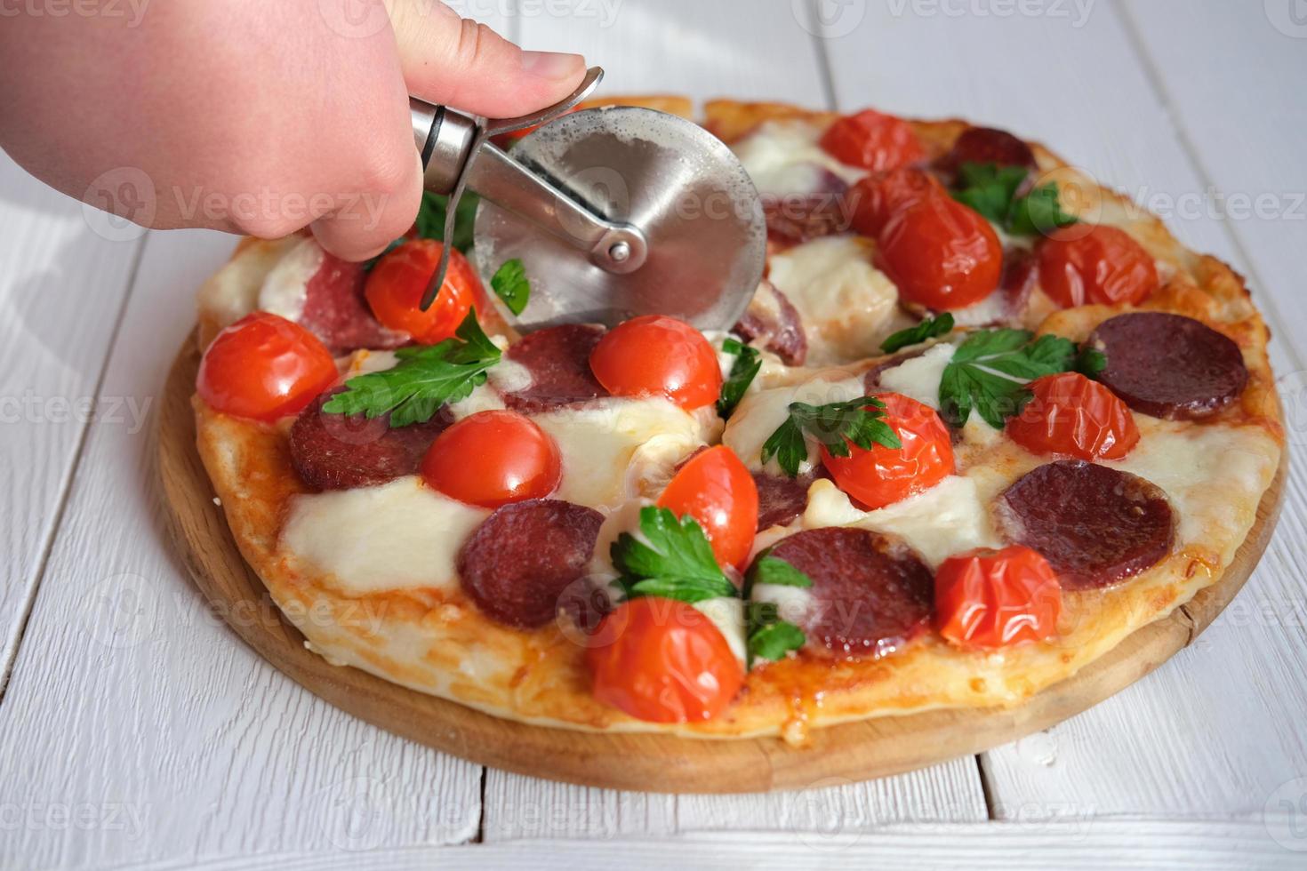 mänsklig hand med pizza cutter skär pizza i köket. foto