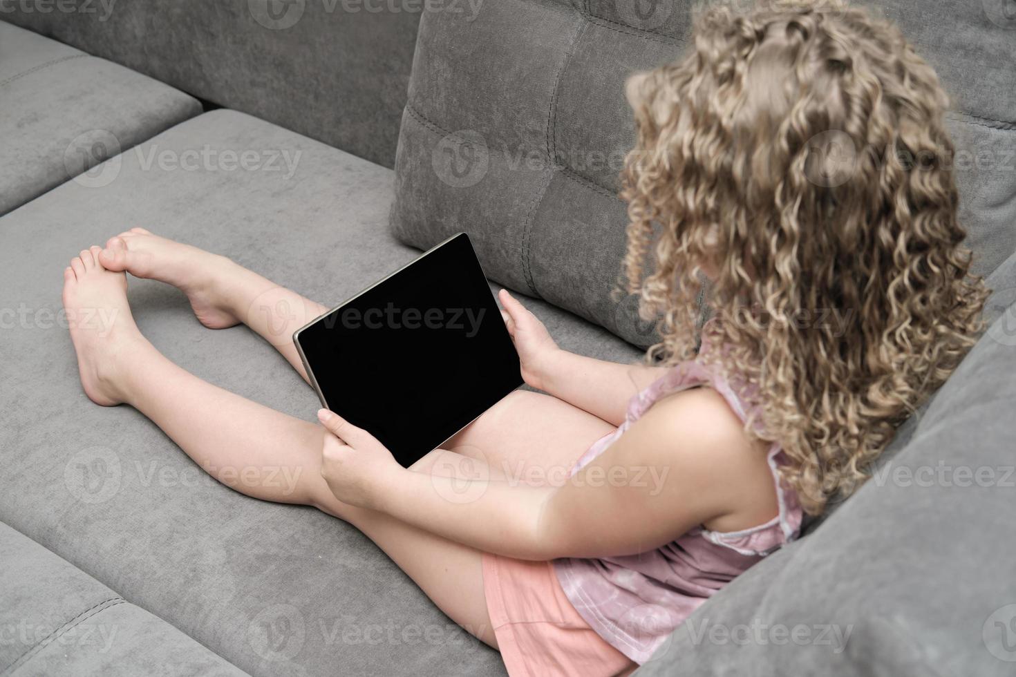 liten flicka som håller en PC-surfplatta och tittar på onlinelektion. foto