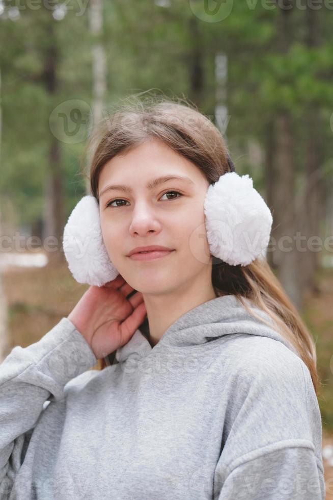 utomhus porträtt av tonåring flicka bär vita hörselkåpor. närbild av en flicka som går i skogen. tonåring tittar på kameran. vandring och spårning ensam. generation z koncept. sidovy foto