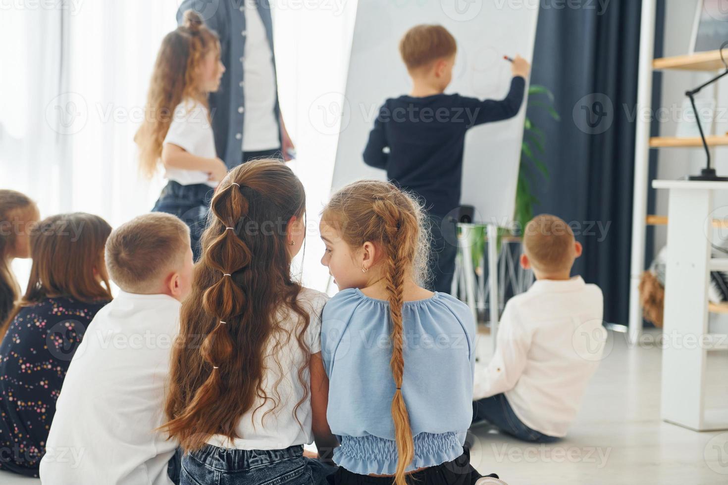 pojke skriver på tavlan. grupp barn elever i klassen i skolan med lärare foto