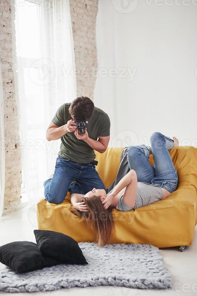 i vardagskläder. fotograf tar en bild av ung flicka som ligger på den vita soffan foto