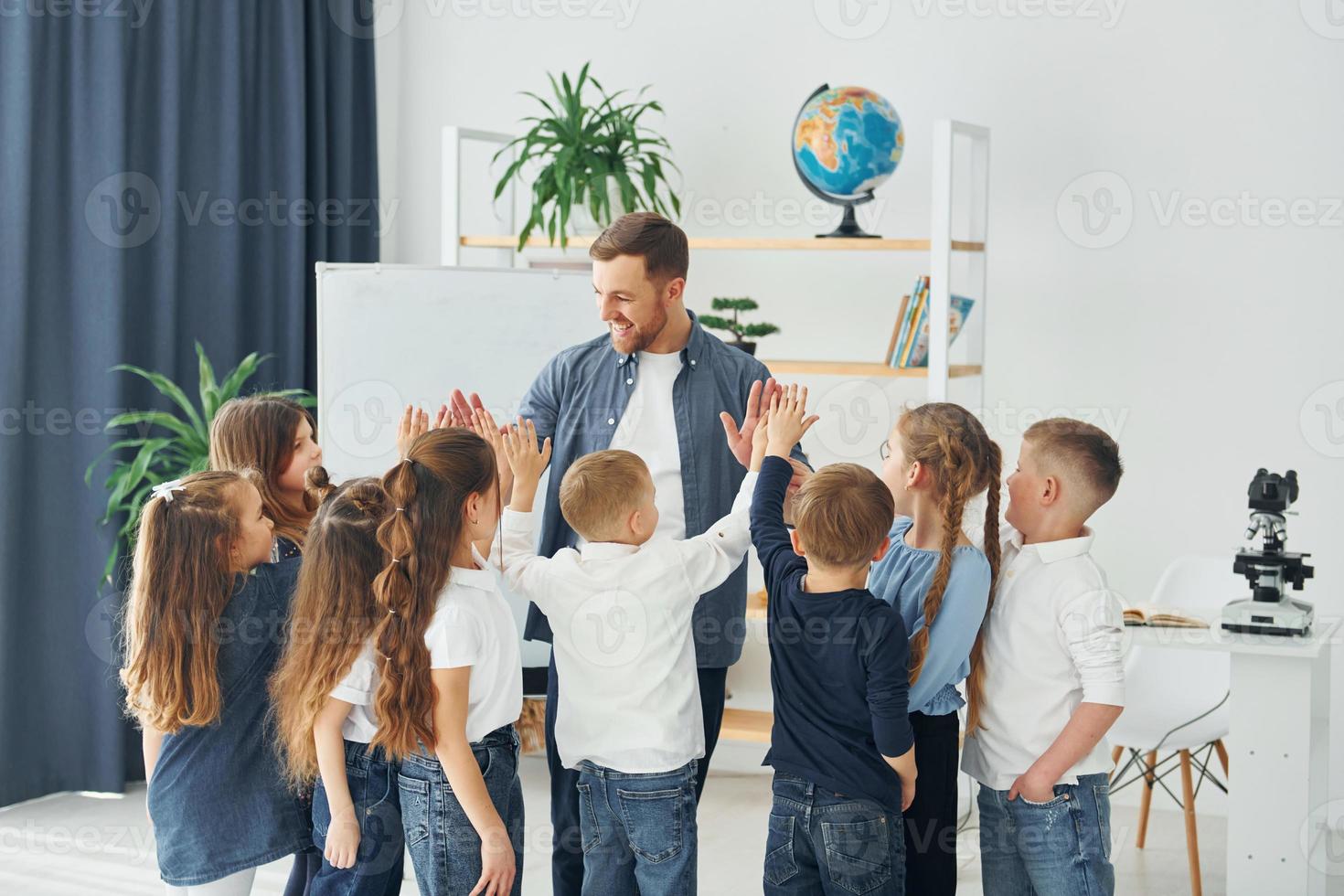 ger high fives i slutet av lektionen. grupp barn elever i klassen i skolan med lärare foto