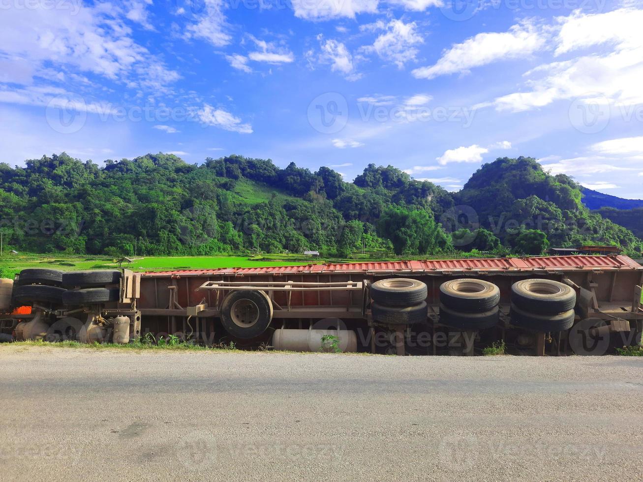 olycksbil faller från väg till grönt risfält med berg och blå himmel. foto