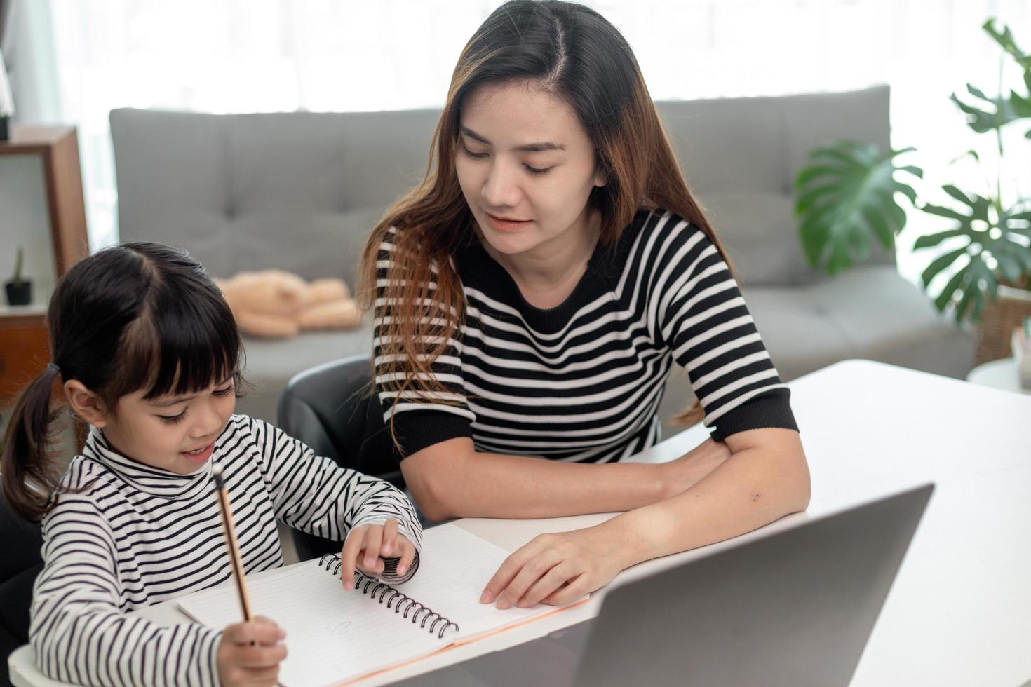 asiatisk liten ung flicka kid lära sig online klass hemma med mamma. förskolebarn använder bärbar dator gör läxor, hemundervisning från skollärare via digitalt fjärrinternet med stöd från mamma. foto