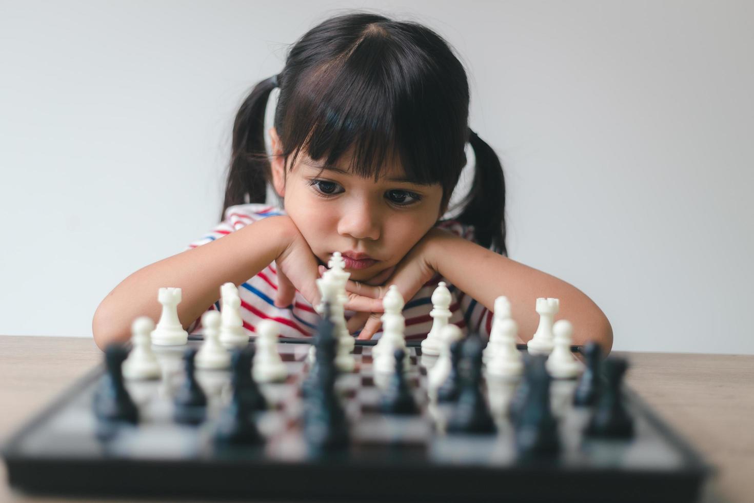 asiatisk liten flicka som spelar schack hemma. ett parti schack foto