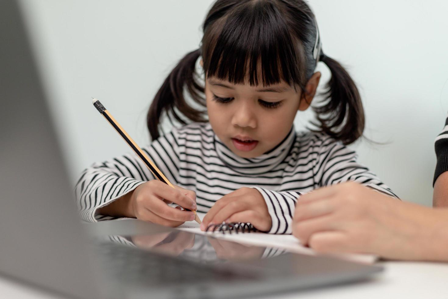 asiatisk liten ung flicka kid lära sig online klass hemma med mamma. förskolebarn använder bärbar dator gör läxor, hemundervisning från skollärare via digitalt fjärrinternet med stöd från mamma. foto