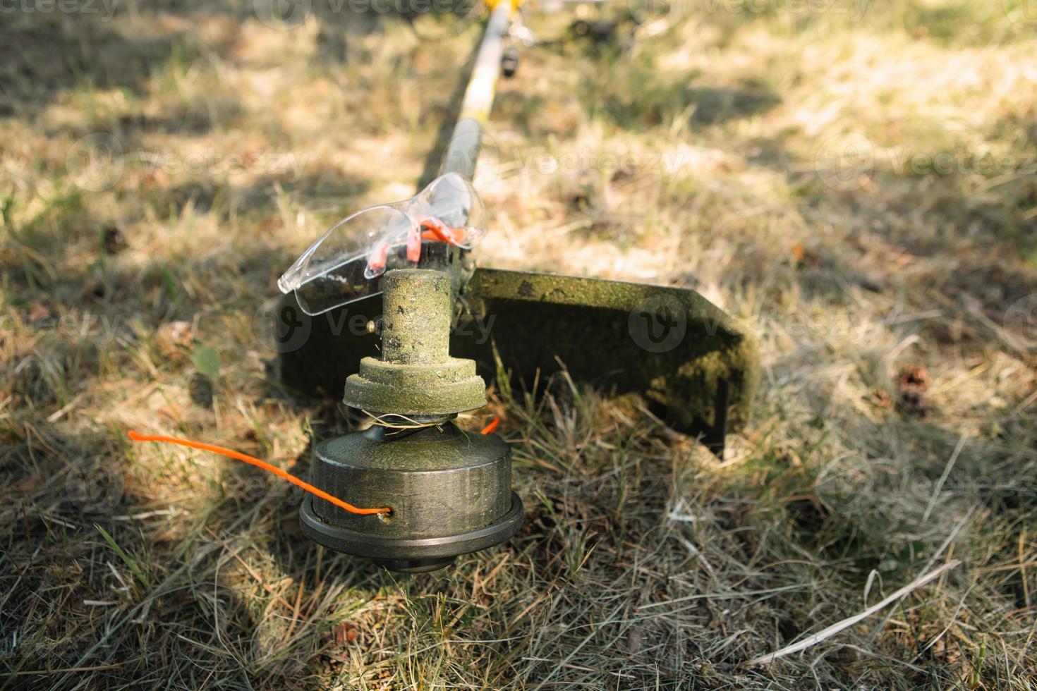 trimmer efter att ha klippt gräs närbild. bensinpump på gräset med skyddsglasögon. trädgårdsskötsel och trädgårdsskötsel av trädgårdstomten, gräsmatta skötsel. foto