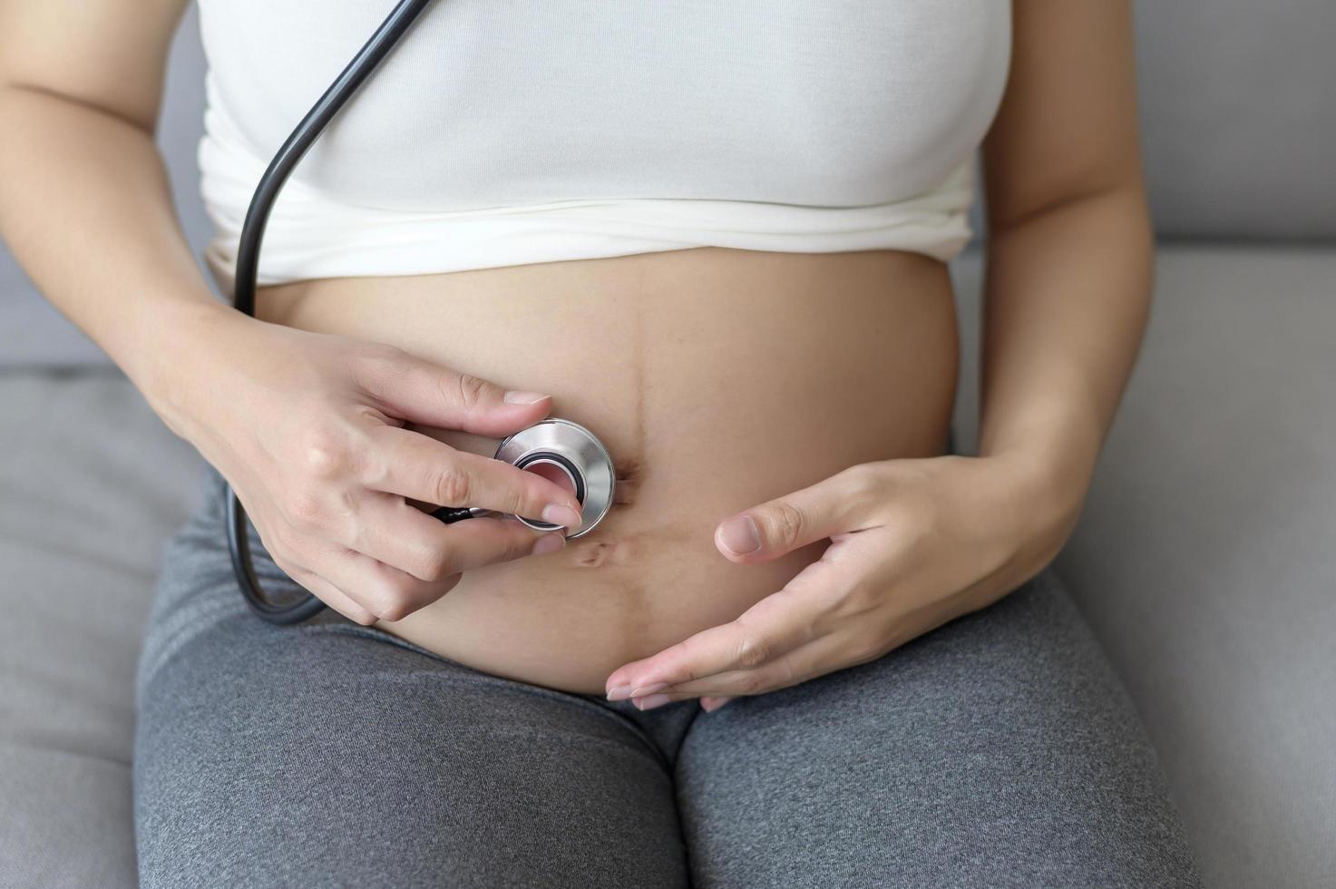 ung gravid kvinna att sätta stetoskop på mage, sjukvård och graviditetsvård koncept foto