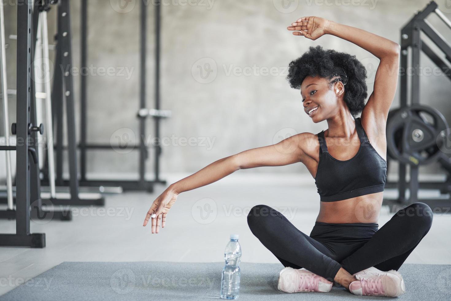 gör några yogasträckor. afrikansk amerikansk kvinna med lockigt hår och i sportiga kläder har träningsdag i gymmet foto