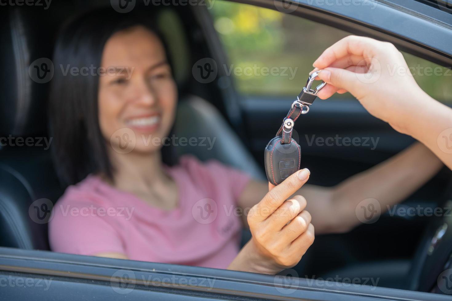 en attraktiv kvinna i en bil får bilnycklarna. hyra eller köp av auto - koncept. professionell säljare under arbete med kund på bilhandlare. ge nycklar till ny bilägare. foto