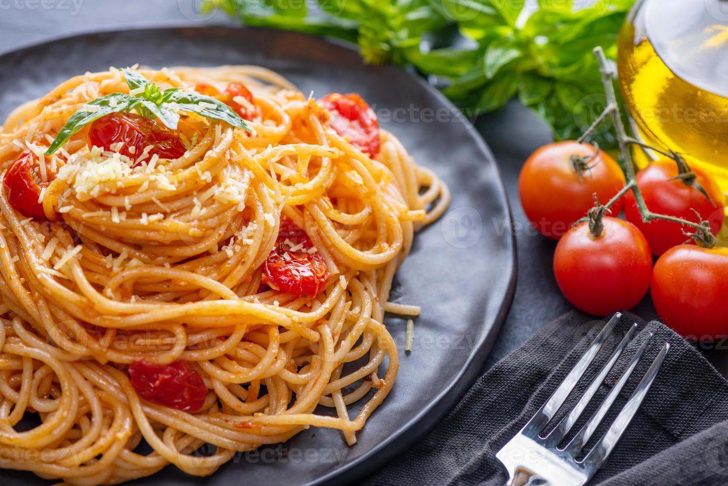 välsmakande aptitretande klassisk italiensk spaghettipasta med tomatsås, ostparmesan och basilika på tallrik och ingredienser för att laga pasta på mörkt bord. foto