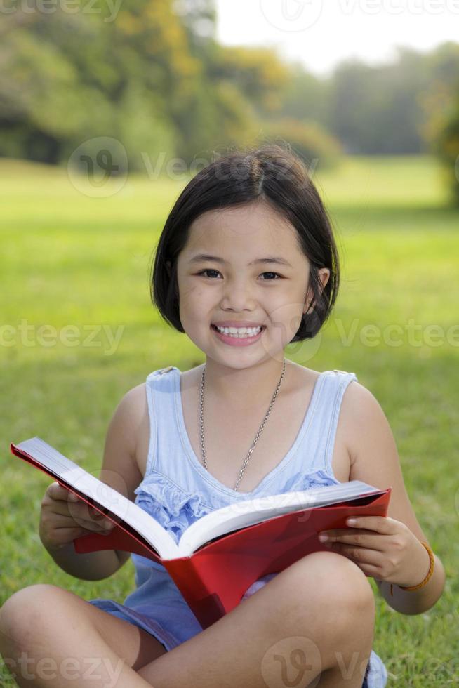 asiatisk liten flicka läser bok i parken foto