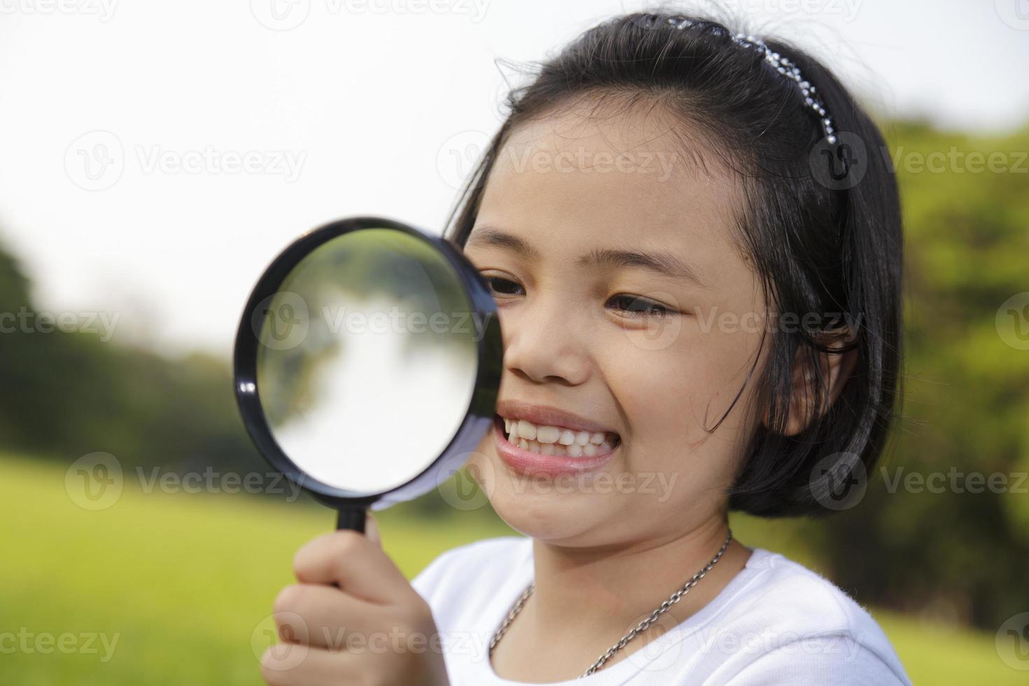 asiatisk liten flicka som håller ett förstoringsglas utomhus foto