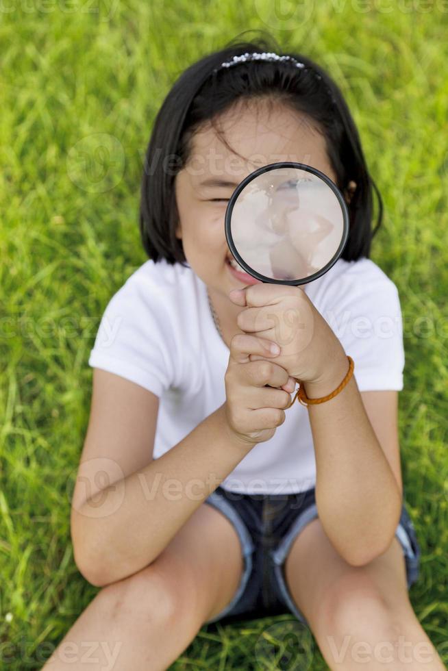 asiatisk liten flicka som håller ett förstoringsglas utomhus foto