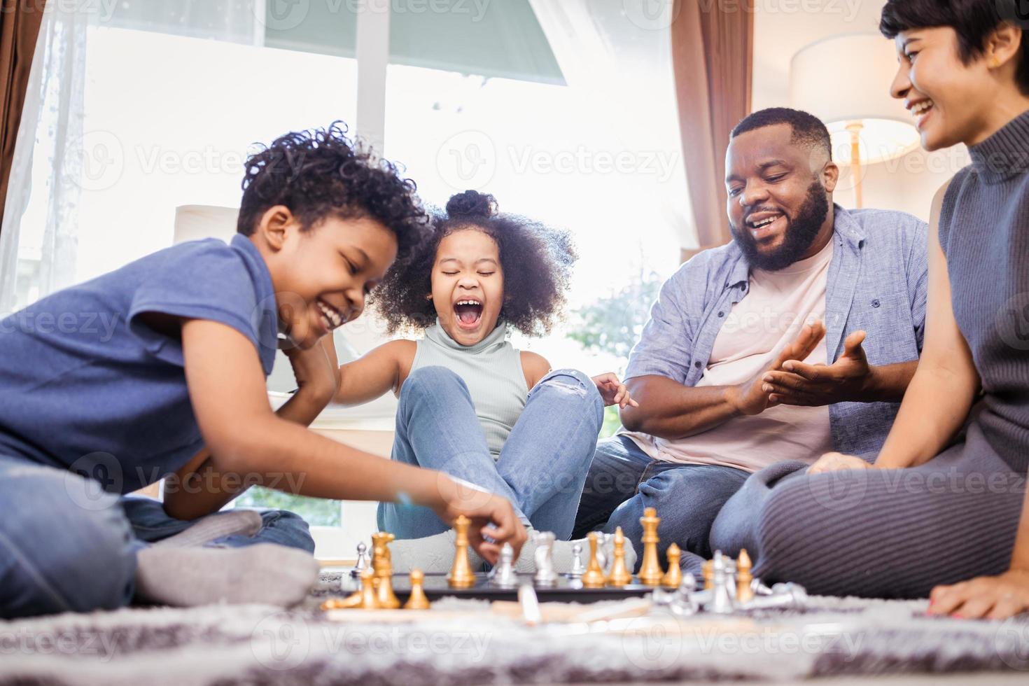 roliga afroamerikanska barn som spelar schack med mamma och pappa hemma foto