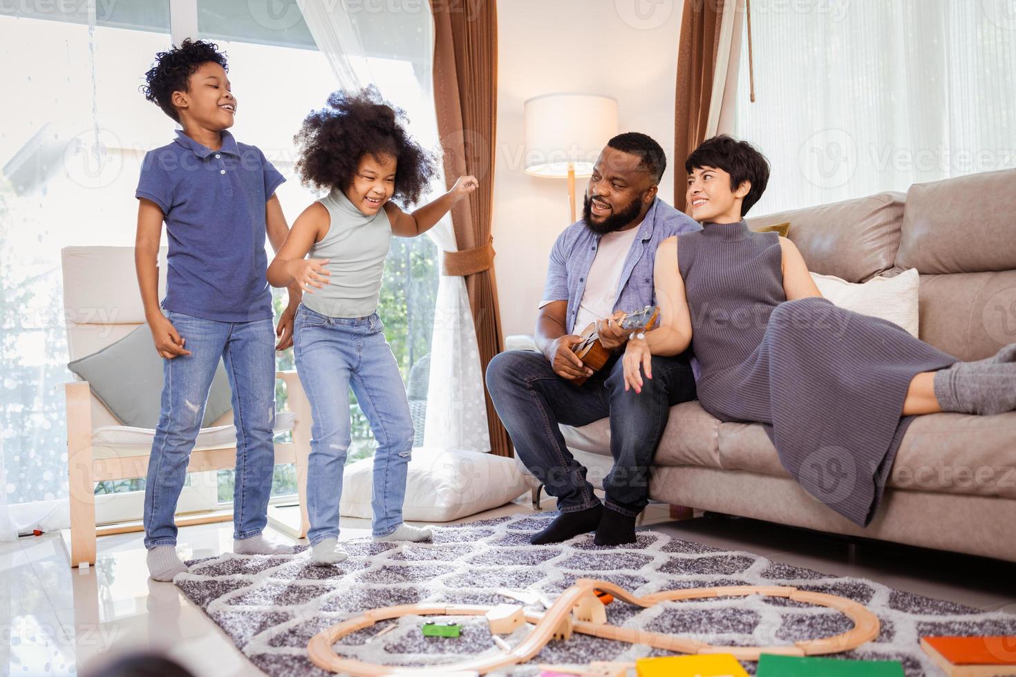 glada afroamerikanska familjeföräldrar med söta barn pojke och flicka dansar i vardagsrummet foto
