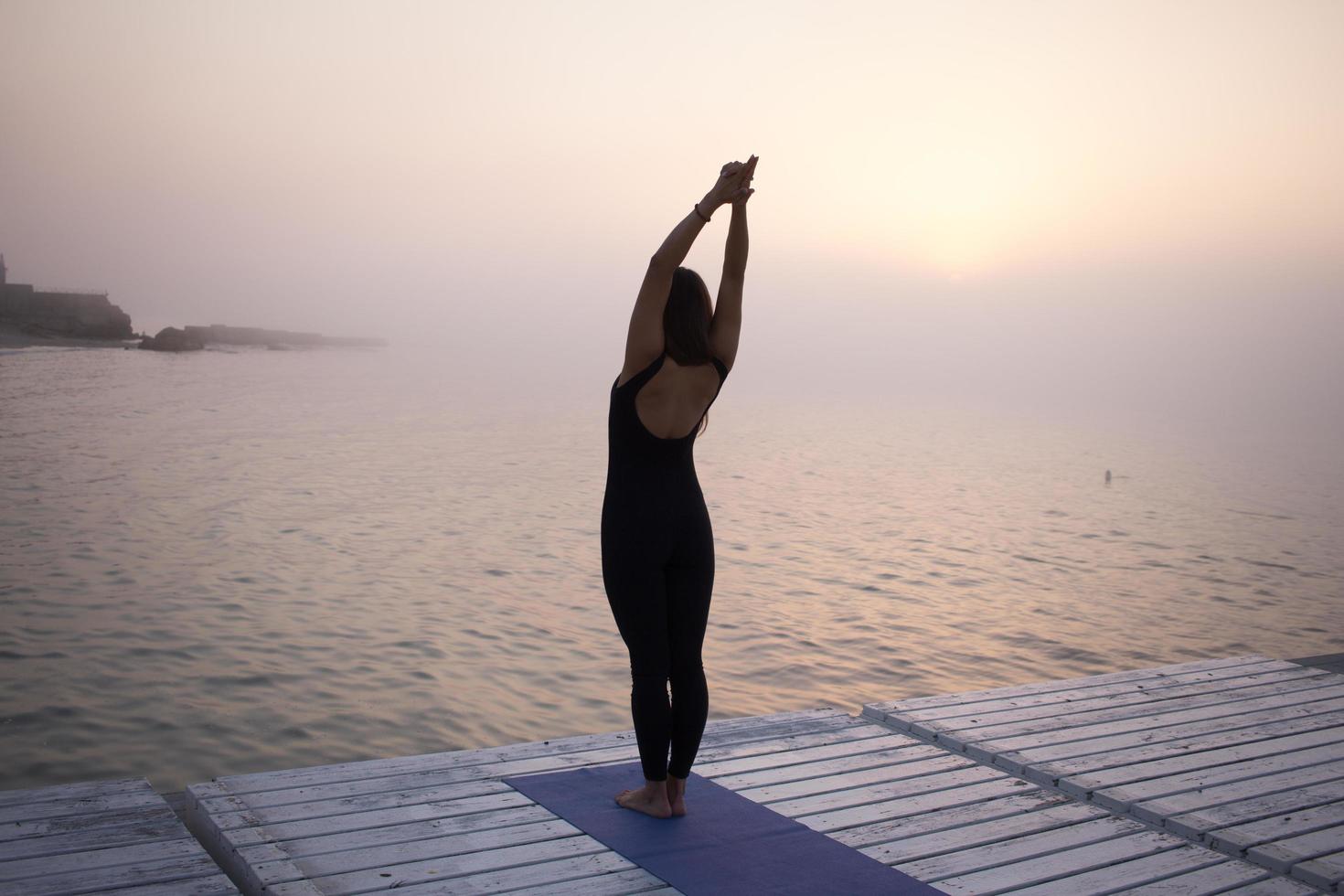 ung kvinna poserar i yoga asans, morgon havet bakgrund foto