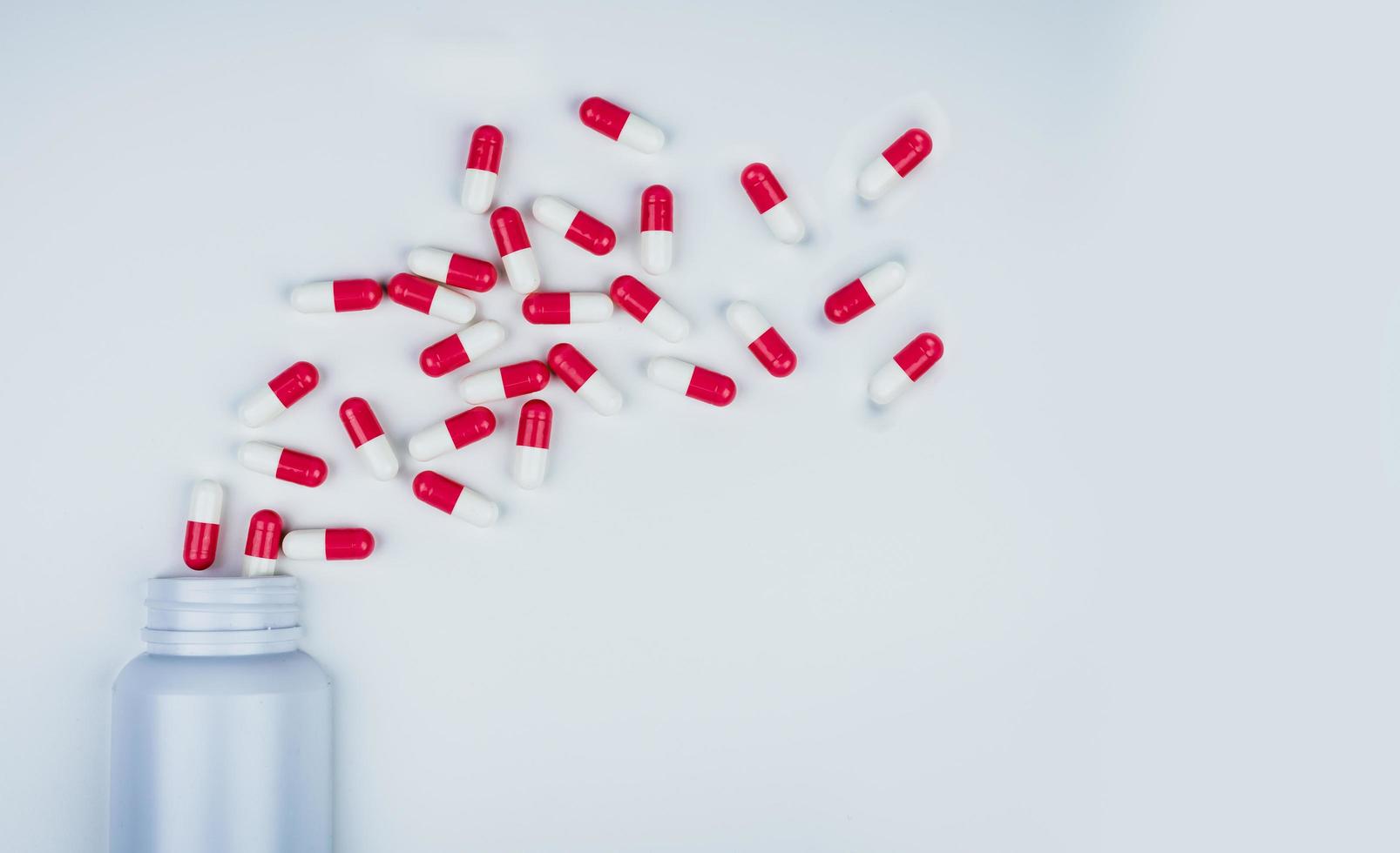 röd-vita antibiotikakapselpiller utspridda ur vit plastflaska. antibiotikaresistenskoncept. användning av antibiotika. global sjukvård. apotek bakgrund. läkemedelsindustri. foto