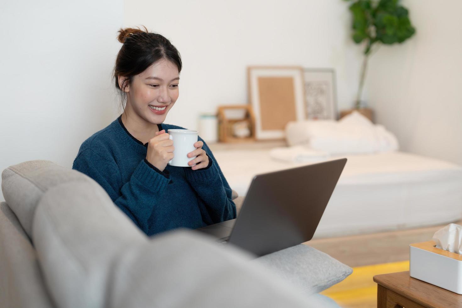 glad vacker kvinna tittar på videor eller online webinar på en bärbar dator som sitter på soffan i huset - online utbildning koncept foto