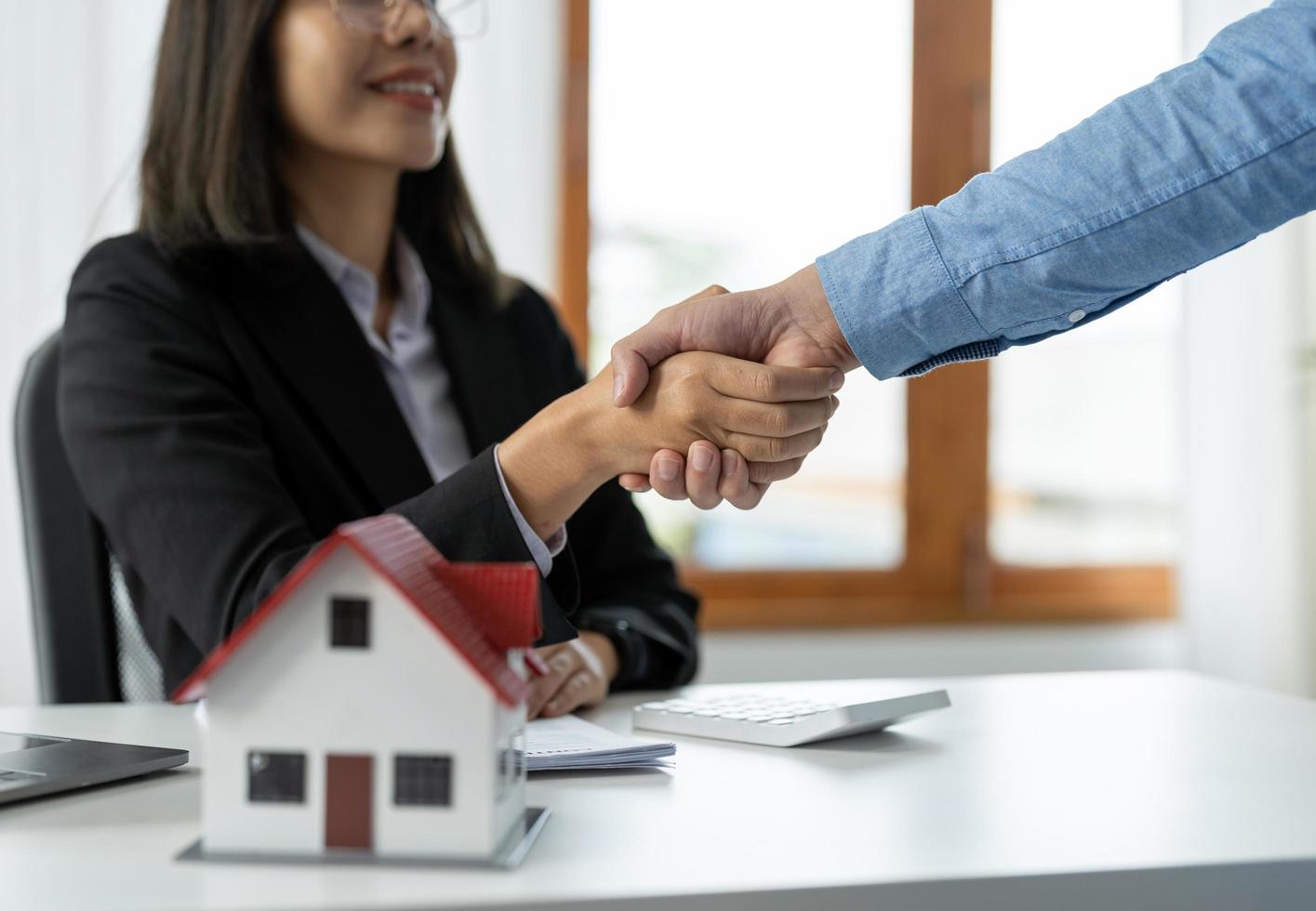 fastighetsmäklare och kunder skakar hand för att gratulera till att ha skrivit på ett kontrakt för att köpa ett hus med mark och försäkring, handslag och bra responskoncept foto