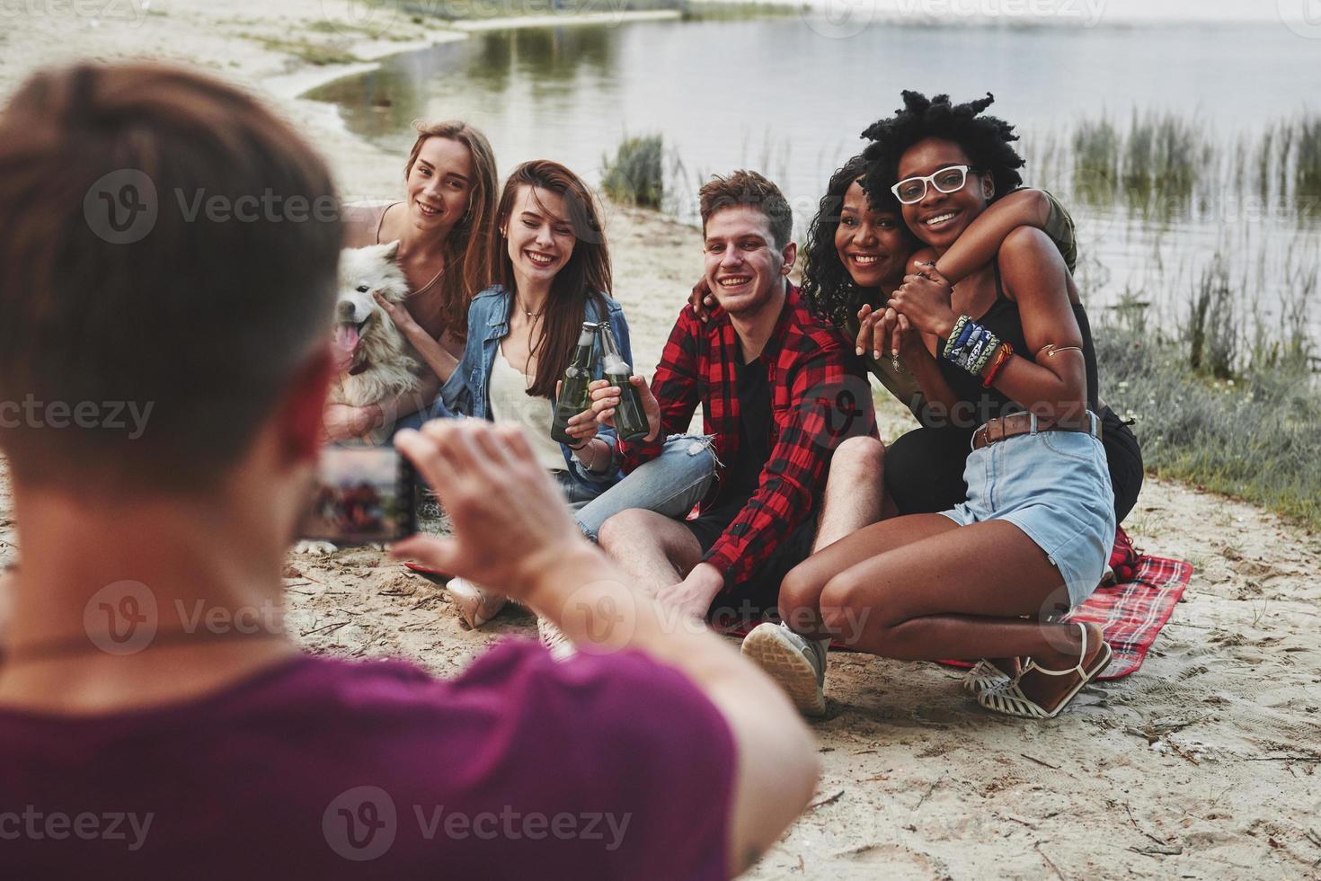 uppriktiga leenden. grupp människor har picknick på stranden. vänner har kul på helgen foto