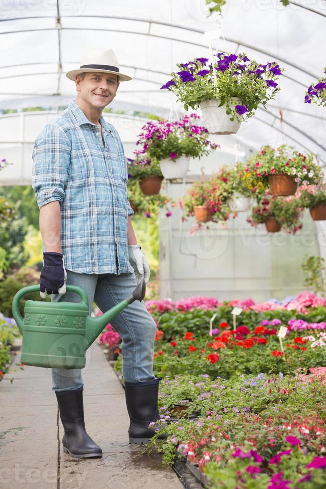porträtt av leende man bär vattenkanna i växthus foto