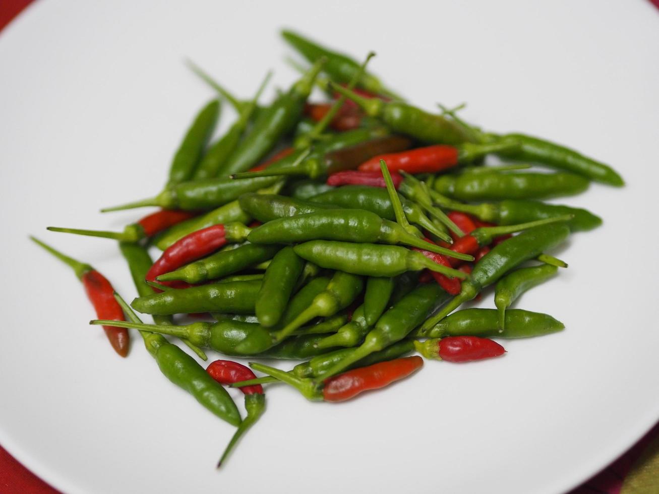 grön röd thai peppar, chili padi, paprika annuum färskhet på vit tallrik grönsaksmat foto