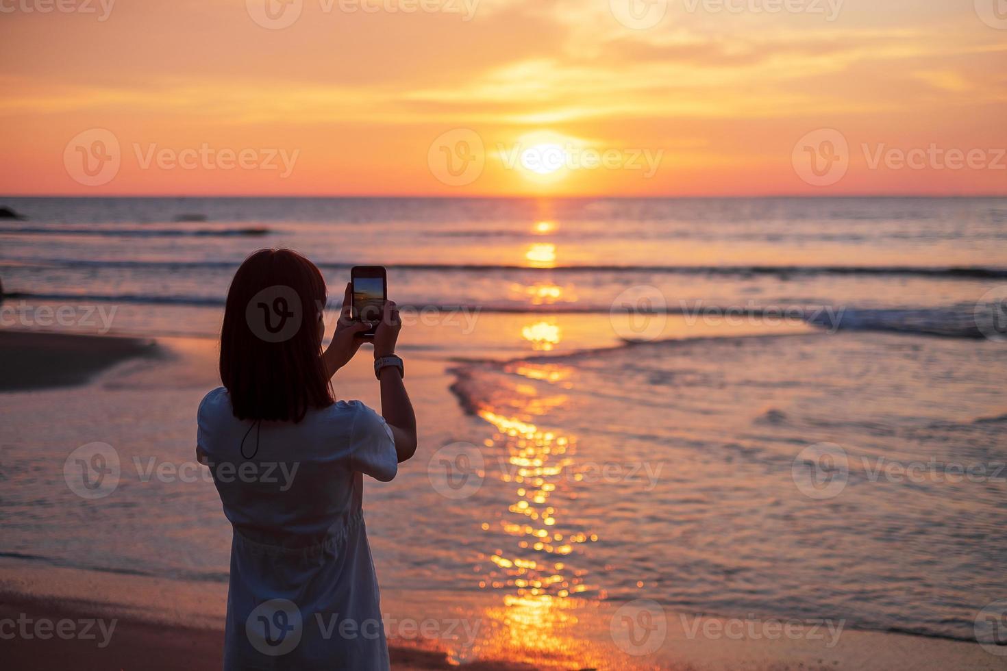 silhuett av glad ung kvinna som tar foto av smartphone.tourist njuta av vacker solnedgång på stranden. resa, avkopplande, semester sommar koncept