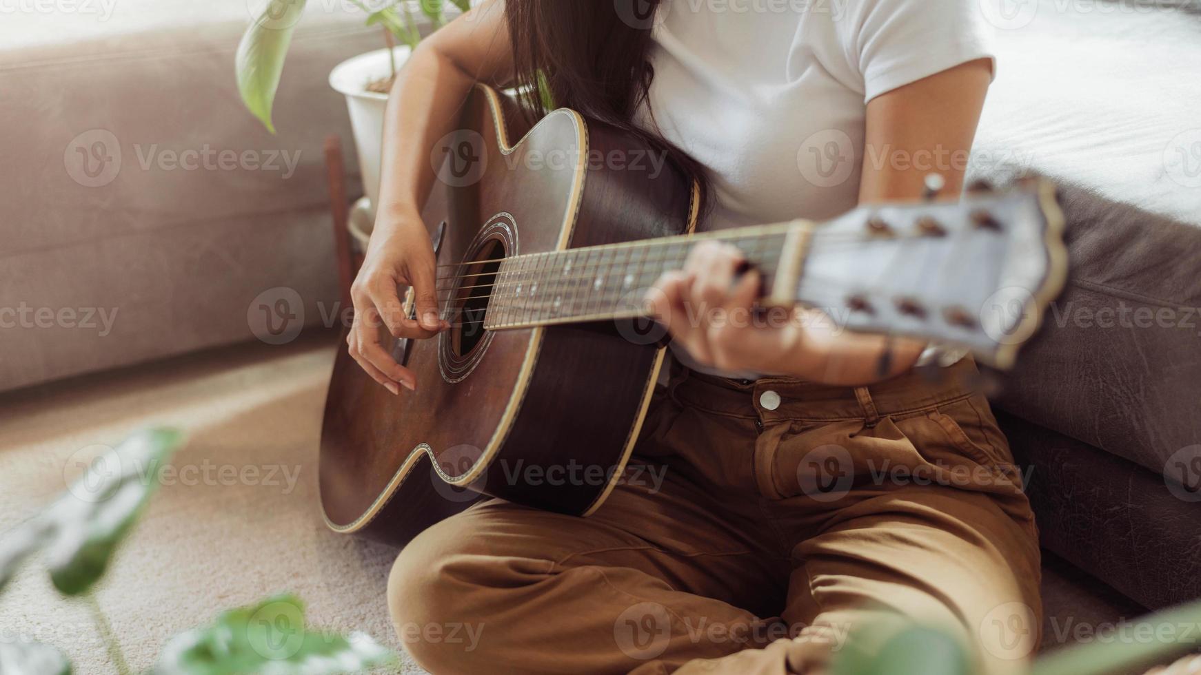 kvinna som spelar gitarr hemma. vacker kvinna ler och spelar gitarr med sina växter i vardagsrummet. foto