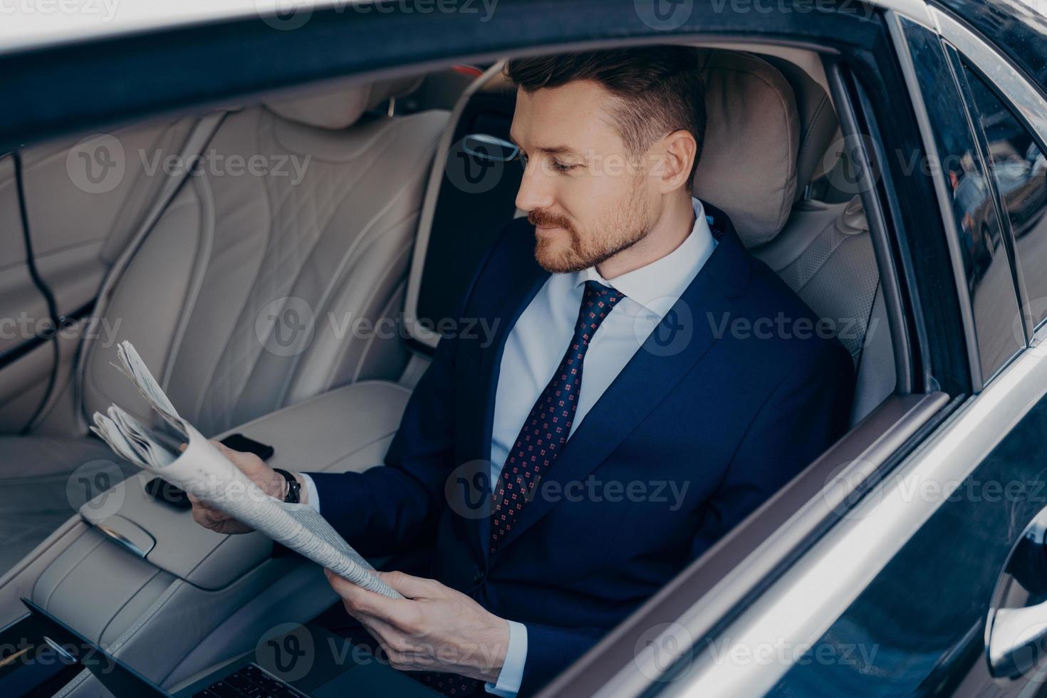 omtänksam verkställande chef i formell kostym läser tidning i baksätet i limousinen foto
