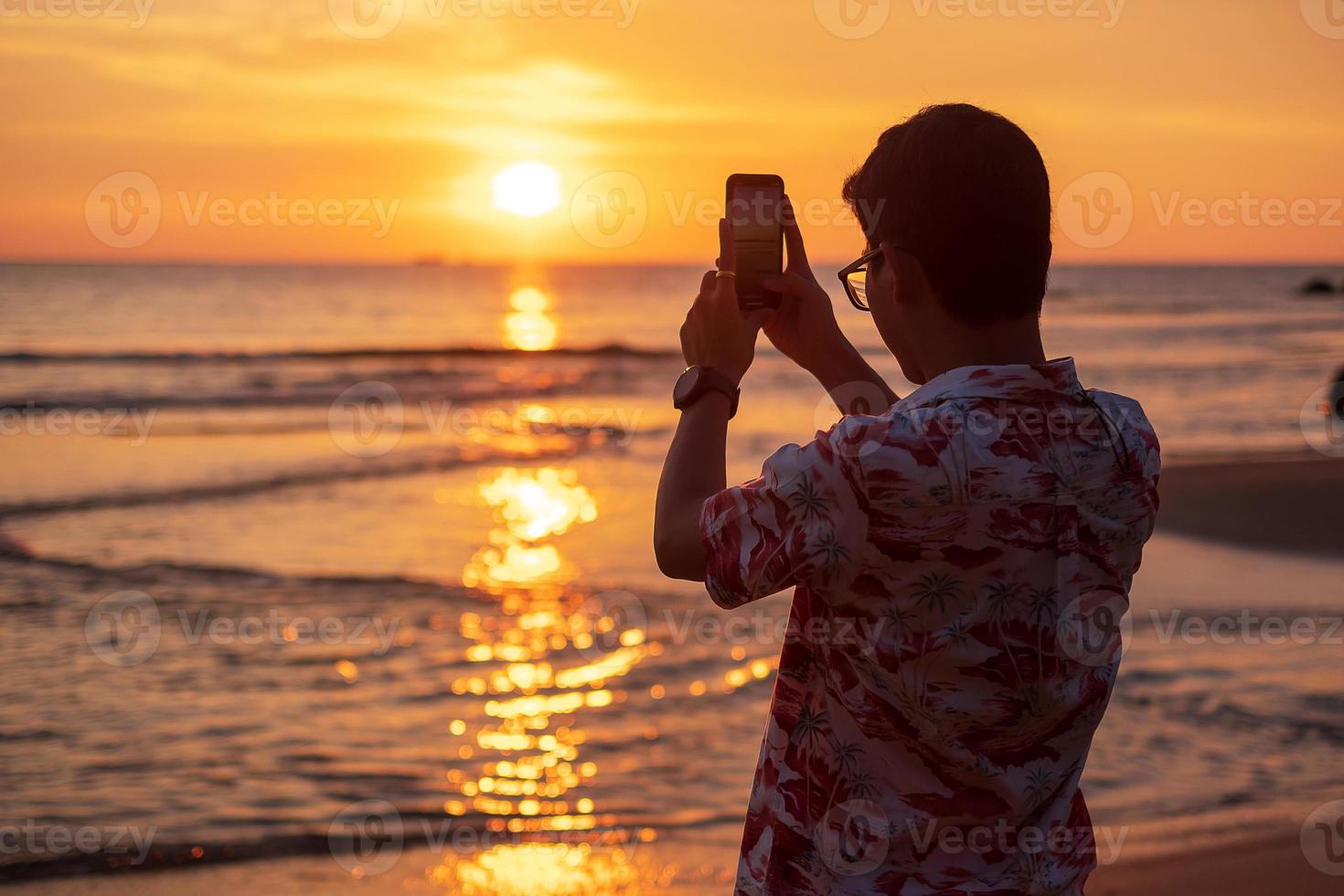 silhuett av glad ung man som tar foto av smartphone.tourist njuta av vacker solnedgång på stranden. resa, avkopplande, semester sommar koncept