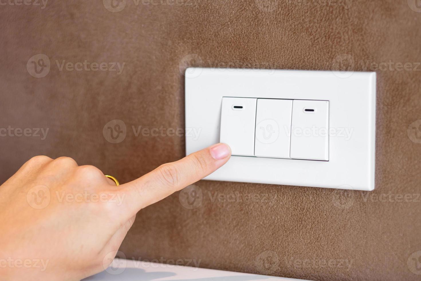 fingret slå på eller av på ljusströmbrytaren på väggen hemma. energibesparing, kraft, el och livsstilskoncept foto
