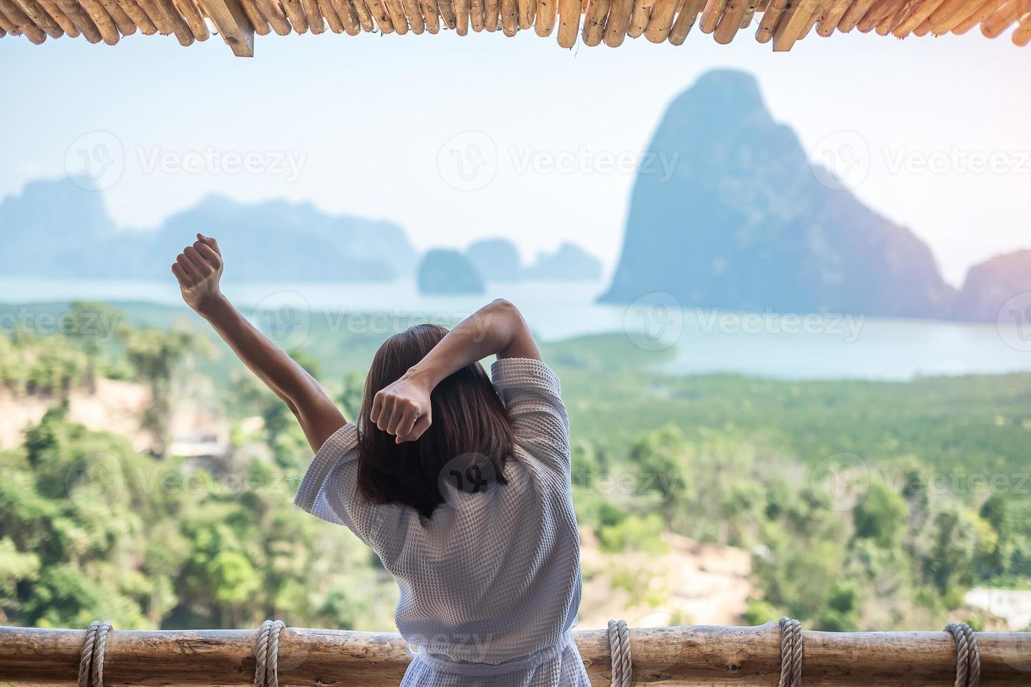 glad kvinna i morgonrock sträcker sig efter att ha vaknat och njut av utsiktspunkten phang nga bay, turist avkopplande i tropisk semesterort på samet nang she, nära phuket i thailand. resor sommar semester koncept foto