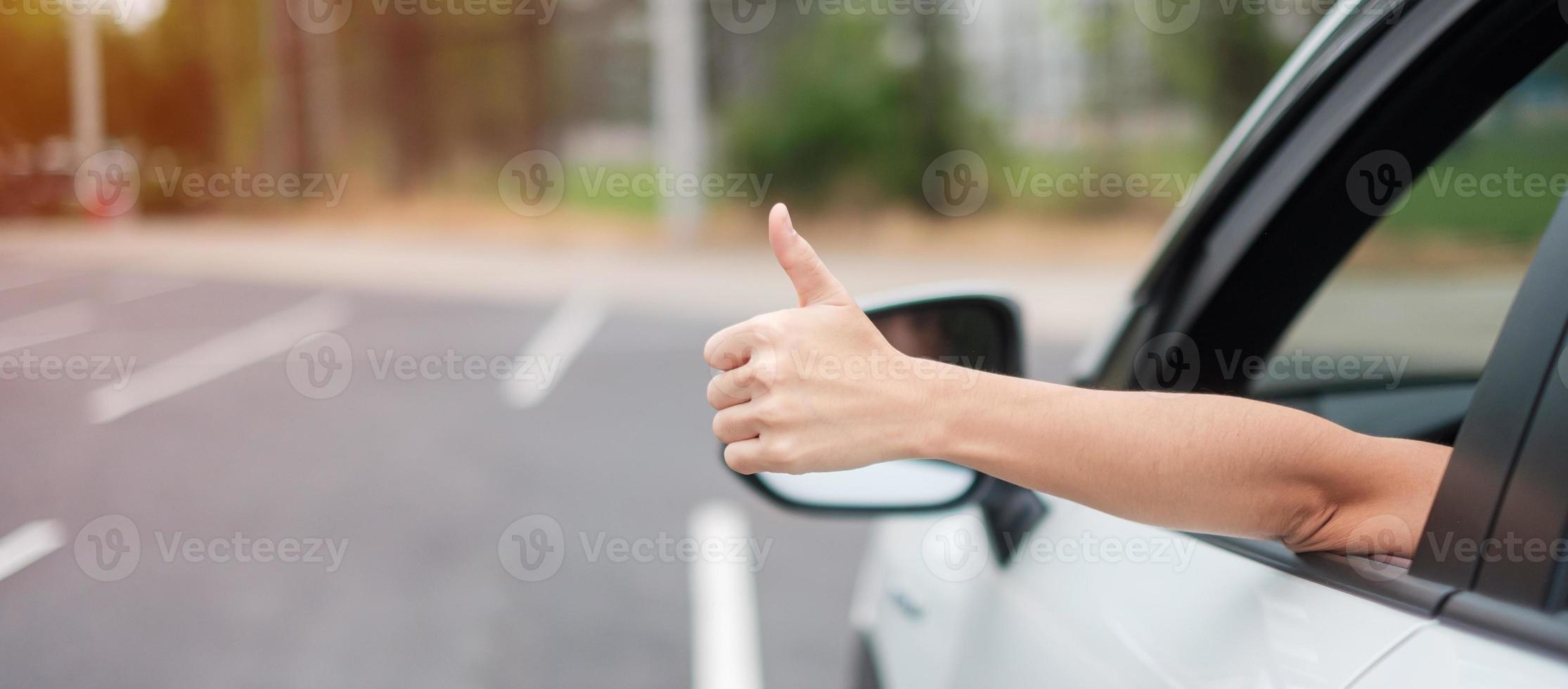 kvinna hand tummen upp under körning av en bil på vägen, handkontrollerande ratt i elektrisk modern bil. resa, resa och säkerhetstransportkoncept foto