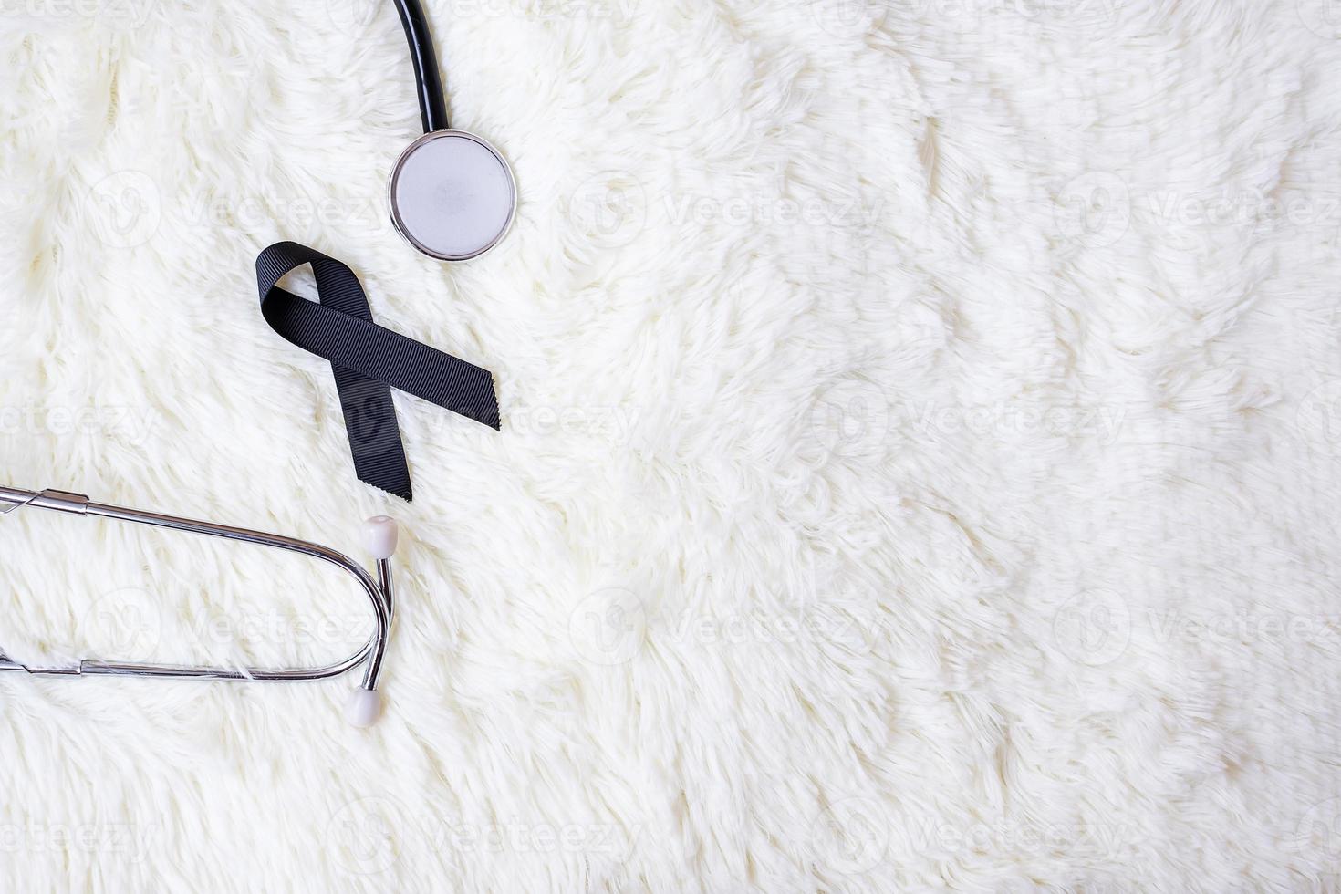 svart band och stetoskop på vit bakgrund. melanom och hudcancer, vaccinskada medvetenhetsmånad och vila i frid-koncept foto