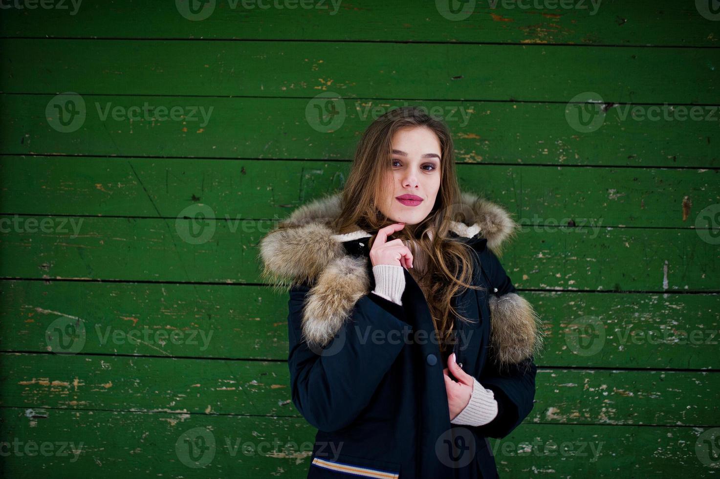 vacker brunett flicka i vinter varma kläder. modell på vinterjacka mot grön träbakgrund. foto