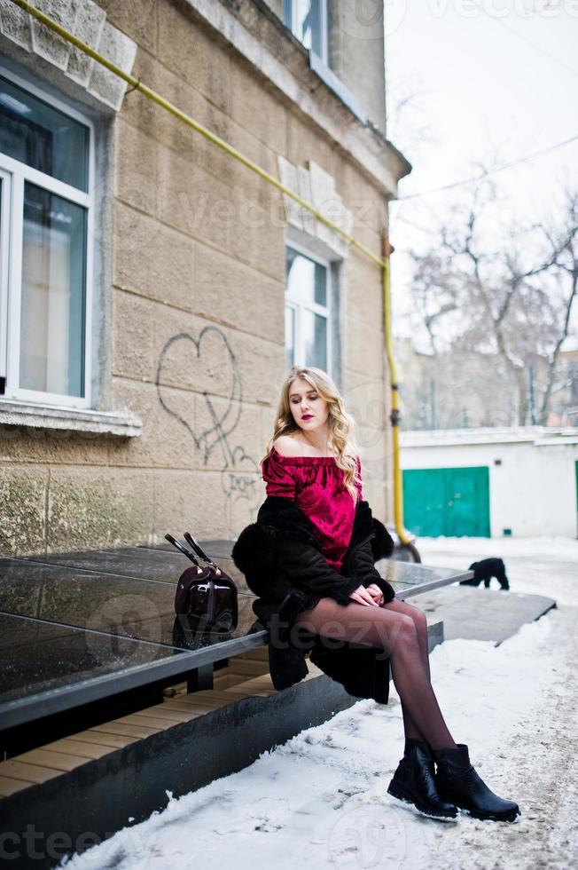 elegans blond flicka i röd frack och päls på gatorna i staden i vinterdag. foto